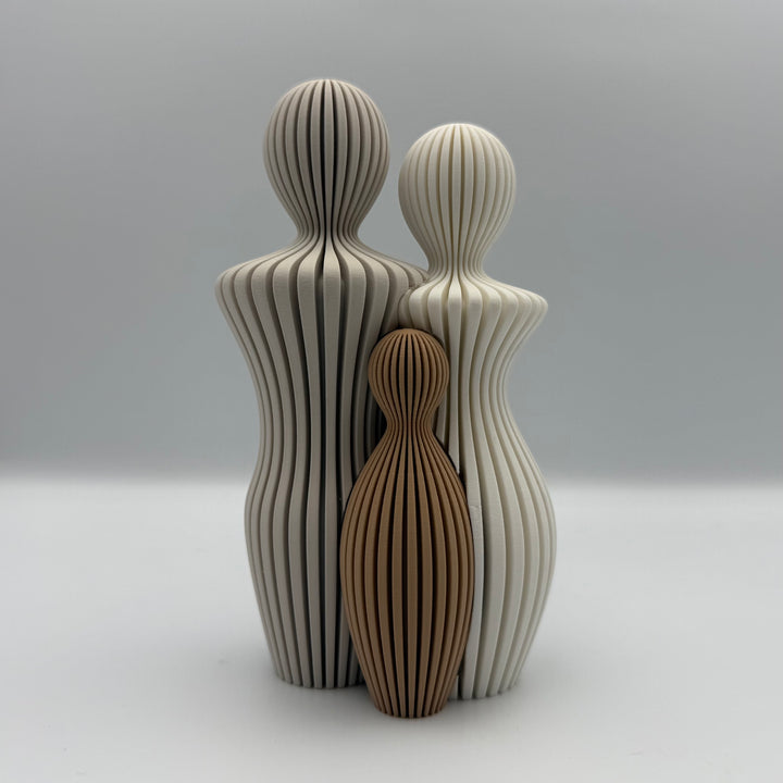 Familien, 3D-printet figur med to lyse voksne og ét brunt barn i ribbet design.
