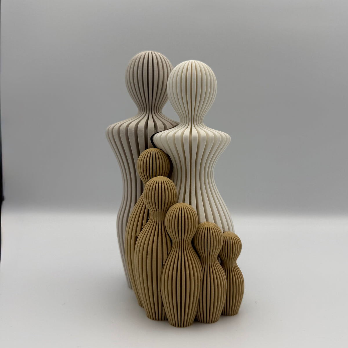 Familien, 3D-printet figur med to lyse voksne og fem gyldenbrune børn i ribbet design.
