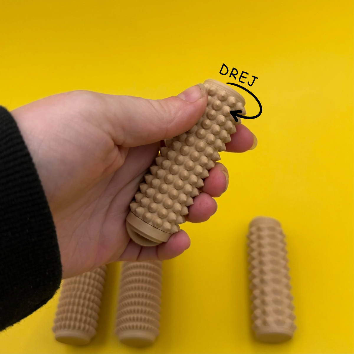 Fidget med drejefunktion og afrundede knopper, vist i en hånd på gul baggrund