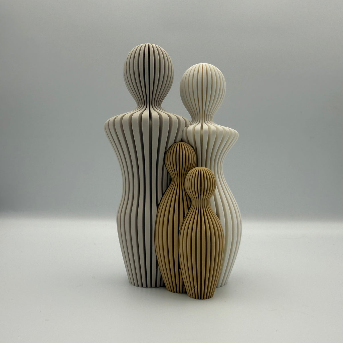 Familien, 3D-printet figur med to lyse voksne og to gyldenbrune børn i ribbet design.
